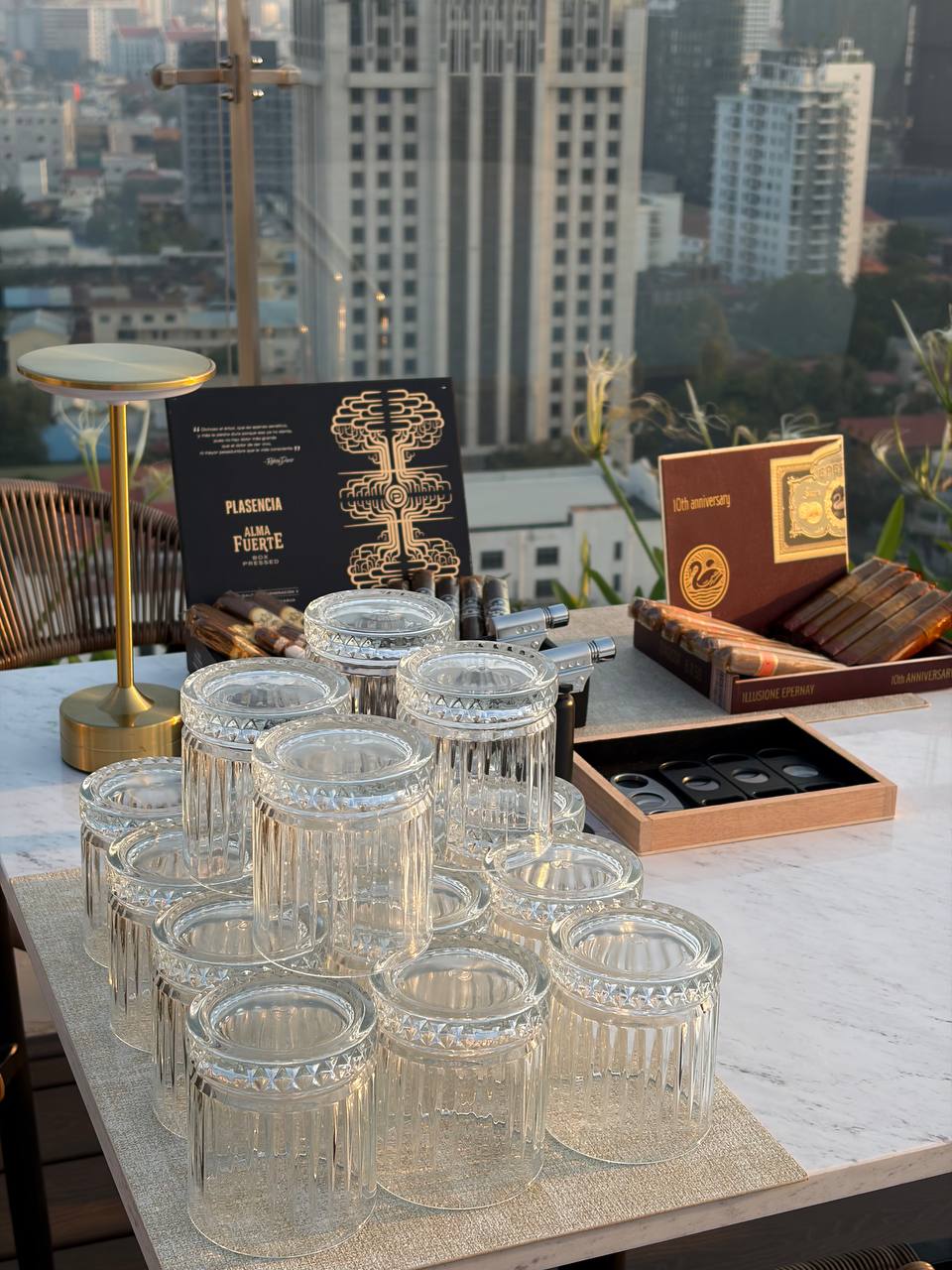 Plasencia cigar setup with crystal glasses and Phnom Penh skyline