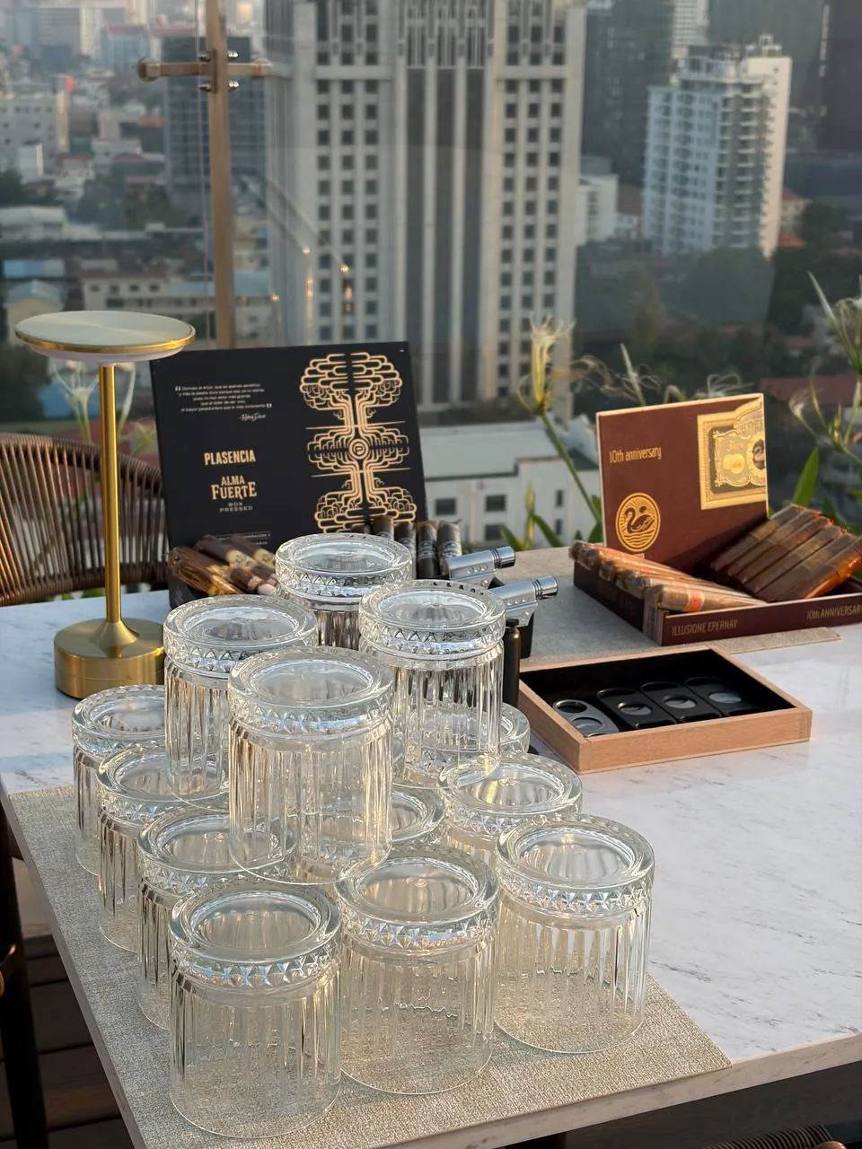 Plasencia cigar setup with crystal glasses and Phnom Penh skyline